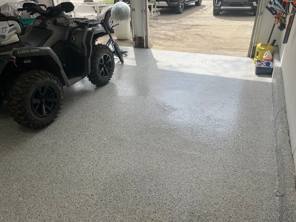 Garage interior with epoxy-coated floor, featuring a Can-Am ATV and organized tools.