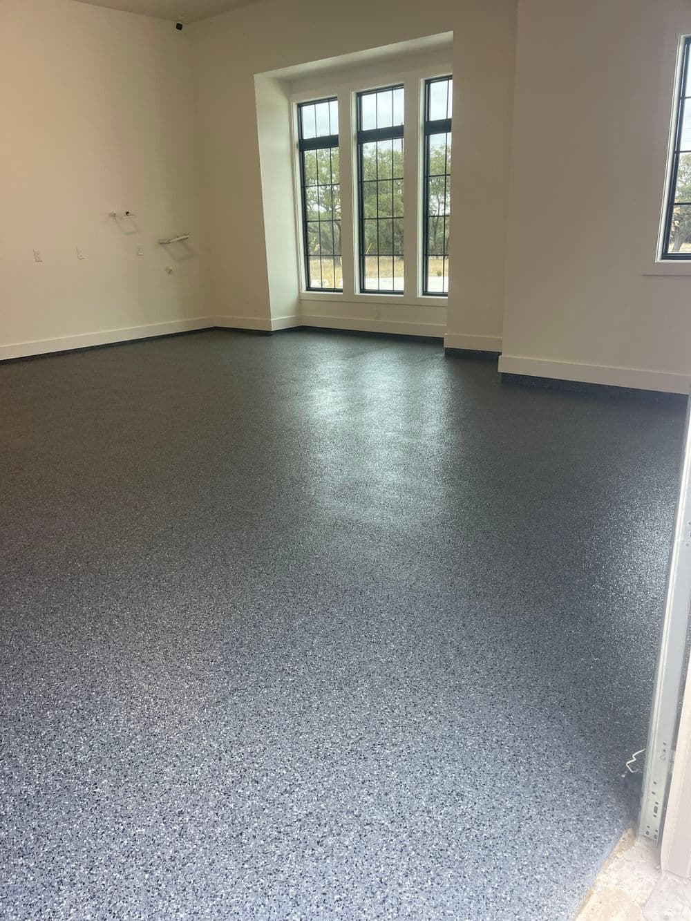 Empty room with blue epoxy floor and large windows, showcasing natural light and spaciousness.